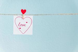 rode Valentijnsdag liefde hart pin opknoping op natuurlijke koord tegen blauwe achtergrond. getekend hart op stuk papier. foto