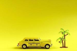 oude retro gele speelgoedautotaxi en speelgoedpalm op gele achtergrond met kopieerruimte. reisconcept foto