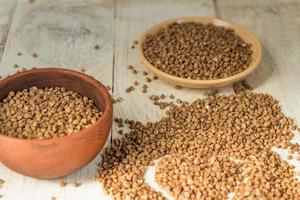 droge boekweit in bruine kleikom op houten tafel. glutenvrije granen voor gezonde voeding foto