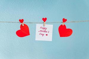 rode liefde harten pinnen opknoping op natuurlijke koord tegen blauwe achtergrond. gelukkige moederdag inscriptie op stuk papier. foto