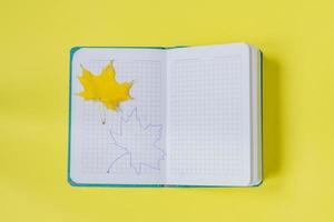 lege notitieblok openen met esdoornblad en tekening op gele achtergrond. leeg dagboek en herfstconcept foto