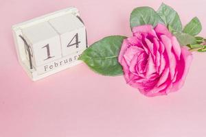 Valentijnsdag en feestdagen concept - close-up van houten kalender met 14 februari datum en pnk roos met waterdruppels foto