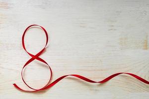 rode geschenk feest lint zwaaide in de vorm van nummer 8 op witte houten achtergrond. wenskaart met kopie ruimte voor 8 maart, internationale vrouwendag foto