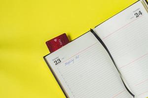 zwarte vrijdag verkoop concept. boodschappenlijstje in notitieboekje en bankkaart als bladwijzer op gele backgrond foto