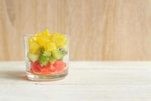 dieet verse smakelijke mix fruitsalade in een glazen pot op houten tafel. gehakte sappige sinaasappels, kiwi en grapefruits. foto