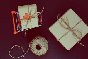 handgemaakte geschenkdozen verpakt in ambachtelijk papier met rood houten hart met touw en boog in winkelwagen, op zwarte achtergrond. bovenaanzicht, plat gelegd foto