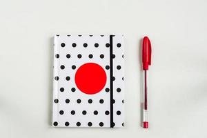 bovenaanzicht van gesloten polka dot cover notebook met rode pen op witte bureauachtergrond foto