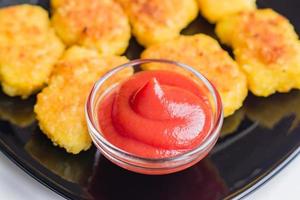 gebakken knapperige kipnuggets met ketchup op zwarte plaat. ongezonde voeding. foto