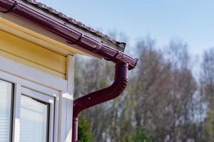 hoek van het huis met goot op een achtergrond van blauwe lucht en lentebos foto