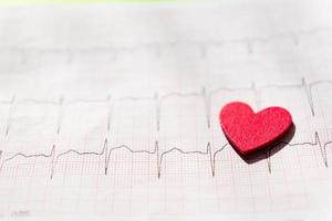 close-up van een elektrocardiogram in papieren vorm met rood houten hart. ecg of ekg papier achtergrondstructuur. medisch en gezondheidszorgconcept.