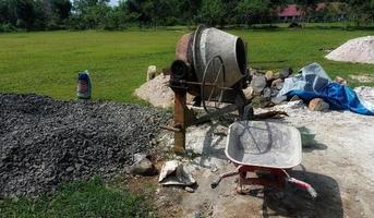 een betonmixer geïnstalleerd op een bouwplaats naast een hoop zand en grind. foto