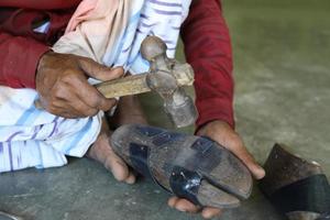 traditionele schoenmaker met hamer die handgemaakte schoenen maakt voor verkoop. close-up van handen van man hameren op leer genageld met een houten frame genaamd laatste. foto