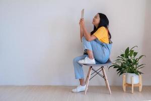 de meisje zittend Aan een stoel Holding een boek in een minimaal kamer. foto