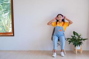 de gelukkig meisje zittend Aan een stoel luisteren naar muziek- in minimaal kamer Bij huis. foto