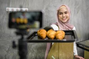 mooi moslim vrouw is maken bakkerij terwijl leven streaming of opname video Aan sociaal media in haar huis, koffie winkel bedrijf concept. foto