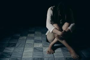 jong persoon vrouw verdrietig, spanning en eenzaamheid zittend in donker kamer, ongelukkig en huilen tiener- meisje van huiselijk geweld, een volwassen vrouw drukt uit gevoelens van wanhoop, ongerustheid van Intimidatie. foto