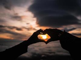 silhouet hart hand- teken met zonsopkomst Aan de berg foto