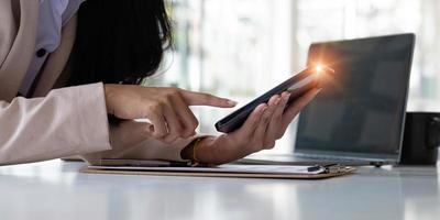 dichtbij omhoog van handen vrouw handen gebruik makend van smartphone terwijl zittend Bij haar kantoor bureau in modern kamer. foto