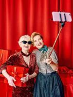 twee senior Dames Bij de partij maken selfie Holding mobiele telefoon Aan selfie stok. partij, viering, technologie concept foto