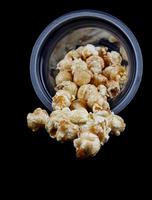 popcorn morsen uit van een plastic glas. isoleren Aan een zwart achtergrond. foto