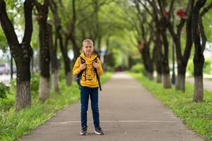 jongen in een geel sweatshirt met een rugzak op zijn rug die naar school gaat. terug naar schoolconcept foto