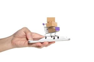 vrouw hand- Holding smartphone met papier dozen in een trolley.online boodschappen doen of ecommmerce concept foto