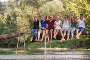 vrienden genieten van watermeloen terwijl zittend Aan de houten brug foto