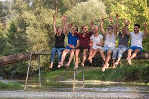 vrienden genieten van watermeloen terwijl zittend Aan de houten brug foto