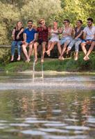 vrienden genieten van watermeloen terwijl zittend Aan de houten brug foto