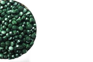 groen tablets gemaakt van natuurlijk biologisch spirulina in een kop Aan een wit achtergrond met vrij ruimte foto