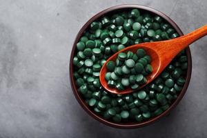 vitamines van spirulina in een houten kop met een houten lepel Aan een donker achtergrond foto