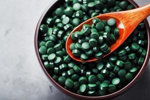 vitamines van spirulina in een houten kop met een houten lepel Aan een donker achtergrond foto