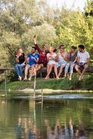 vrienden genieten van watermeloen terwijl zittend Aan de houten brug foto