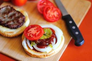 de Hamburger is wezen bereid en geserveerd met gesneden tomaten, uien, augurken. Aan een houten snijdend bord in de keuken foto