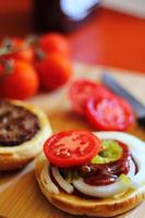 de Hamburger is wezen bereid en geserveerd met gesneden tomaten, uien, augurken. Aan een houten snijdend bord in de keuken foto