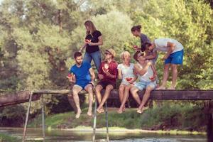 vrienden genieten van watermeloen terwijl zittend Aan de houten brug foto