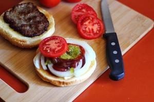 de Hamburger is wezen bereid en geserveerd met gesneden tomaten, uien, augurken. Aan een houten snijdend bord in de keuken foto