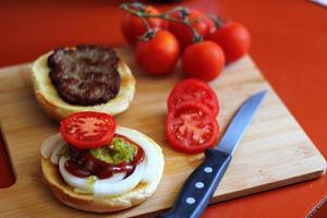 de Hamburger is wezen bereid en geserveerd met gesneden tomaten, uien, augurken. Aan een houten snijdend bord in de keuken foto