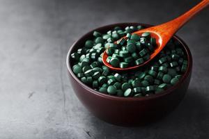 vitamines van spirulina in een houten kop met een houten lepel Aan een donker achtergrond foto