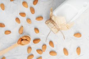 melk van biologisch amandelen in een transparant fles met een verstrooiing van zaden en een houten lepel Aan een licht achtergrond foto