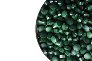 groen tablets gemaakt van natuurlijk biologisch spirulina in een kop Aan een wit achtergrond met vrij ruimte foto