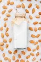 amandel melk in een fles omringd door een verstrooiing van amandel zaden Aan een licht achtergrond foto