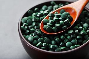 biologisch spirulina tablets in een houten kop met een houten lepel foto