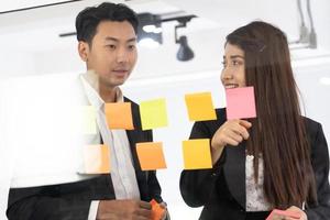 mensen uit het bedrijfsleven kantoor arbeider lezing kleverig aantekeningen Aan planning glas bord. bedrijf team richten Aan trefwoorden in kleverig aantekeningen en bedrijf verslag doen van naar brainstorming over planning strategie van bedrijf. foto