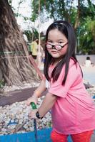 portret schattig Aziatisch meisje is spelen een scooter. gelukkig kind slijtage bril. kind in roze is spelen in de speelplaats. kinderen zijn 6 jaren oud. foto