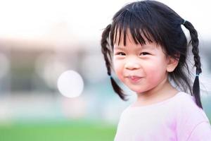 portret van Aziatisch gezicht kind meisje zoet glimlach. gelukkig kind met wazig bokeh achtergrond in de avond. schattig baby met zwart haar- gevlochten twee vlechtjes Aan elk kant. kopiëren ruimte. foto