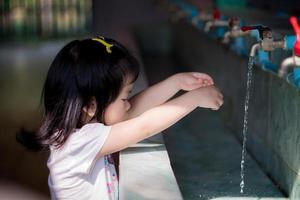 meisje bereiken uit naar wassen handen in wasbak, opening de kraan naar laat water rennen door haar hand. kind is geïnteresseerd in stromen van water.kinderen is op zoek water dat hits de goot vloer.kid schoon handen foto