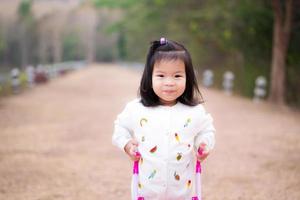 schattig Aziatisch meisje zijn zoet glimlacht, vervelend wit truien voor wandelen in natuurlijk park. kind duwt de roze kar Aan bruin aarde weg. concept van kinderen aan het leren over natuur in de omgeving van. baby is 3 jaren oud. foto