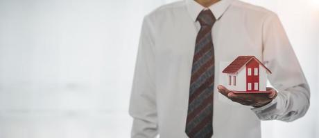 bedrijf persoon handen Holding huis model, klein gebouw rood huis. echt landgoed agenten aanbod contracten naar aankoop of huur residentieel. hypotheek eigendom verzekering in beweging huis en echt landgoed concept foto