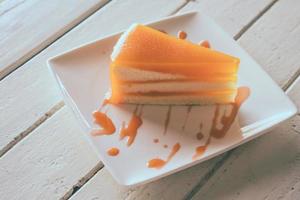 oranje taart in wit schotel Aan de hout tafel. foto